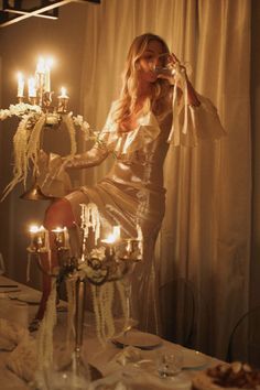 a woman sitting on top of a table next to a chandelier filled with candles