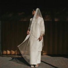 a woman in a white dress and veil is walking down the street with her hands on her hips