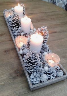 pine cones and candles are arranged in a tray on a wooden table with other decorations