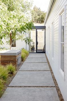 a walkway leading to a white house with black doors and windows by an open door