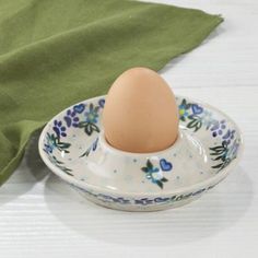 an egg sitting in a small bowl on top of a table next to a green napkin