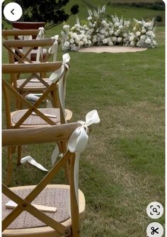 chairs with bows on them sitting in the grass near flowers and an area that looks like it has been set up for a wedding