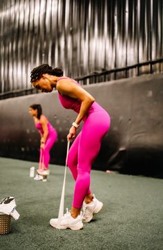 two women in pink are playing golf on an indoor court, one is holding a club and the other is wearing white shoes