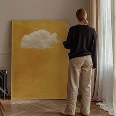 a woman standing in front of a large yellow cloud on a wall next to a window