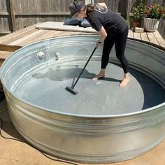 a woman in black shirt and hat cleaning an outdoor pool with a mop on it