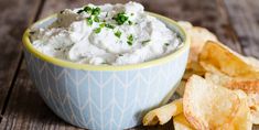 a blue bowl filled with white dip next to chips on a wooden table and a spoon