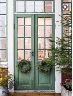 two wreaths are on the front door of a house with green doors and windows