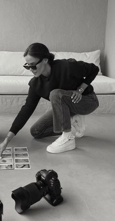 a black and white photo of a woman kneeling on the floor with her camera in hand