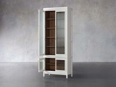 a tall white cabinet with glass doors on the top and bottom shelves, in front of a concrete wall