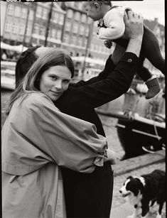 a woman holding a baby in her arms next to a dog on the dock with other dogs