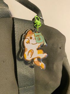 a cat shaped keychain hanging from the side of a gray bag with a green strap