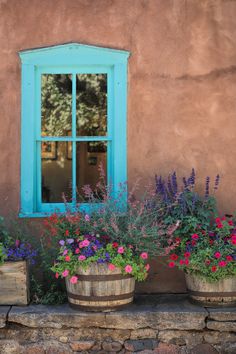 two wooden buckets filled with flowers sitting next to a window on a stone wall