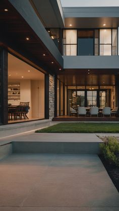 a modern house is lit up at night with the lights on and lawn in front