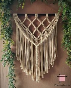 a macrame hanging on the wall next to some green plants and ivys