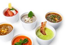 five different types of soups in white bowls on a white surface with garnishes