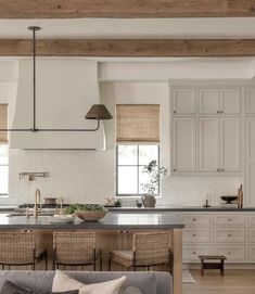 a large kitchen with white cabinets and wooden beams in the ceiling, along with wicker chairs