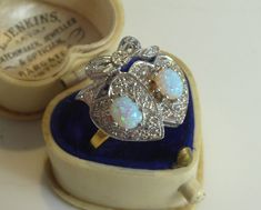 This beautiful Edwardian Style Ring is a unique piece of fine jewellery that will add elegance to any outfit. Crafted from solid silver with 18ct gold plating, it features stunning Oval cut cultured Opal  stones Surrounded with Clear Cubic Zirconia all within a Double Sweetheart bow Topped Mount Setting  as the main attraction. The ring is available in size 7.25 and is perfect for collectors and lovers of fine jewellery. The colour of the ring is gold, and the base metal is silver, making it a v Yellow Gold Hallmarked Opal Ring For Gift, Yellow Gold Hallmarked Opal Ring As A Gift, Yellow Gold Opal Ring Hallmarked As Gift, Victorian Heart-shaped Anniversary Rings, Art Deco Diamond Ring With 17 Jewels For Gift, Gold Opal Ring With Brilliant Cut As Gift, Gold Opal Ring With Brilliant Cut For Gift, Heart Cut Hallmarked Jewelry For Wedding, Fine Jewelry Hallmarked Opal Ring Gift