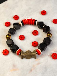 Size: ((Medium)) Bead Sizes: 10mm-14mm Primary Colors: Black, Red, White, Gold Cord: Black Stretch 1mm 1 Pcs The Warrior King is inspired by the many conquering kings of the ancient times. West African rulers of the Igbo, Yoruba, Dahomey, Mandinka were often enemies but they had bravery in common.  African Bead bracelet handmade with African glass, wood, brass, hematite and other materials. Our beads are sourced globally but most of our products are made with handmade African materials. Trade beads are older than written history. We wish to keep the tradition alive and bring it into the modern age. Made with elastic cord. Bracelets are meant to be rolled onto the wrist, not stretched. Jewelry care is important. Black Wooden Beads Bracelet For Gift, Black Bracelets With Large Beads For Gift, Black Bracelets With Large Beads As Gift, Red Wooden Bead Bracelets, Red Wooden Round Bead Bracelets, Red Wooden Round Beads Bracelet, Red Bracelets With Black Round Beads, Red Stretch Bracelet With Black Beads As A Gift, Red Stretch Bracelet With Black Beads