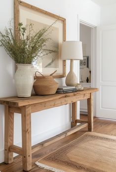 a wooden table topped with a vase filled with flowers next to a lamp and painting