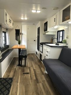 the interior of a mobile home with wood flooring and white cabinets, black counter tops, and gray couch