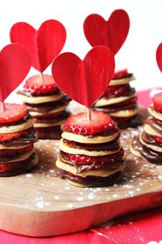 some heart shaped cookies are sitting on a cutting board with strawberries in the shape of hearts