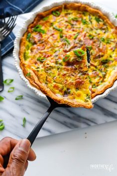 a person holding a spoon with a quiche in it on top of a table