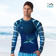 a man standing in front of the ocean wearing a blue shirt with a fish on it