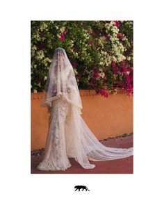 a woman in a wedding dress with a veil on her head and flowers behind her