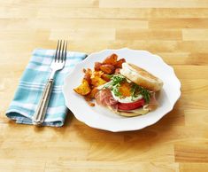 a white plate topped with a sandwich next to a fork and knife on top of a wooden table