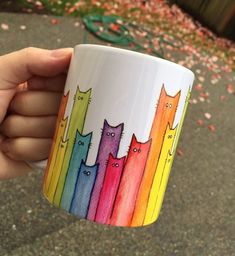 a hand holding a coffee cup with cats painted on the side and rainbow colored stripes