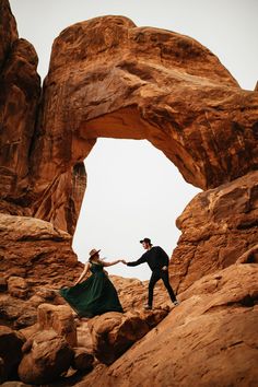 a man and woman holding hands in front of an arch shaped rock formation at the desert