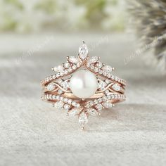 a close up of a ring with pearls and diamonds on it, next to a pine tree