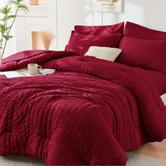 a bed with red comforter and pillows in a room next to a potted plant