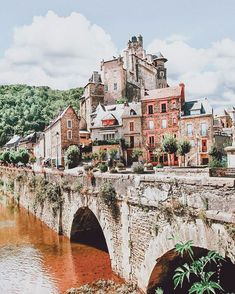 an old stone bridge over a river with buildings on the other side and trees in the background