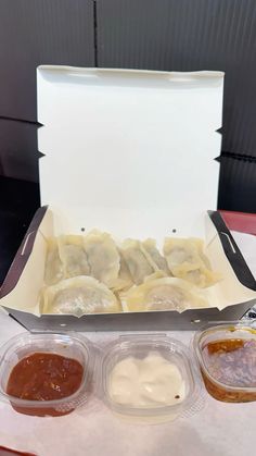 an open take out box filled with dumplings and sauces