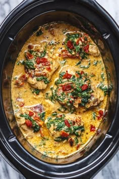 a crock pot filled with chicken, spinach and tomato sauce in the slow cooker