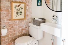 a white toilet sitting next to a bathroom sink under a mirror on a brick wall