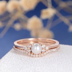 a pearl and diamond ring sitting on top of a white cloth with flowers in the background