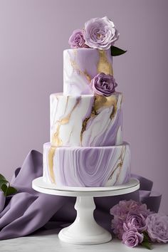 a three tiered cake with purple flowers and gold leaf decoration on top, sitting on a white pedestal