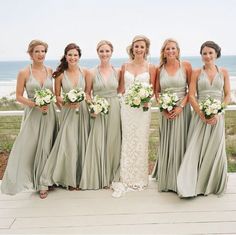 a group of women standing next to each other near the ocean with bouquets in their hands