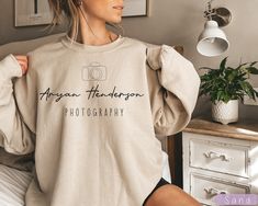 a woman sitting on top of a bed wearing a sweater that says, always the photographer