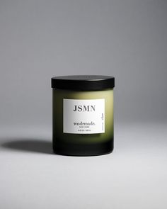 a candle that is sitting on a table next to a gray background with the words jsmn written in it