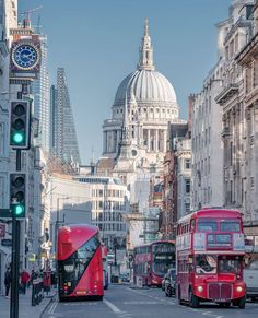 two red double decker buses driving down a street next to tall buildings and a clock tower