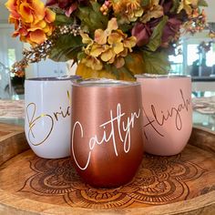 three hand painted wine glasses sitting on top of a wooden tray with flowers in the background