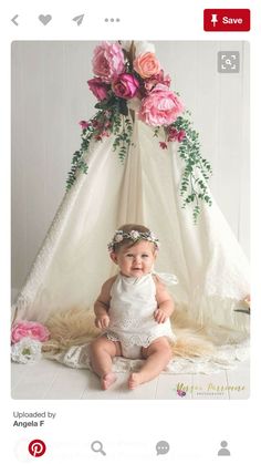 a baby sitting in front of a teepee with flowers on it's head