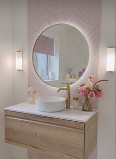 a bathroom vanity with a round mirror above it and flowers in vases on the counter