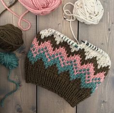 a knitted purse sitting on top of a wooden floor next to balls of yarn