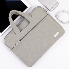 a gray purse sitting on top of a white table next to an ipad and headphones