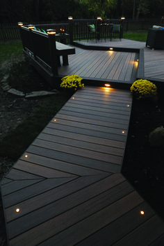 a wooden deck with lights on it and flowers in the grass next to it at night