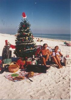 two people sitting in lawn chairs next to a christmas tree on the beach